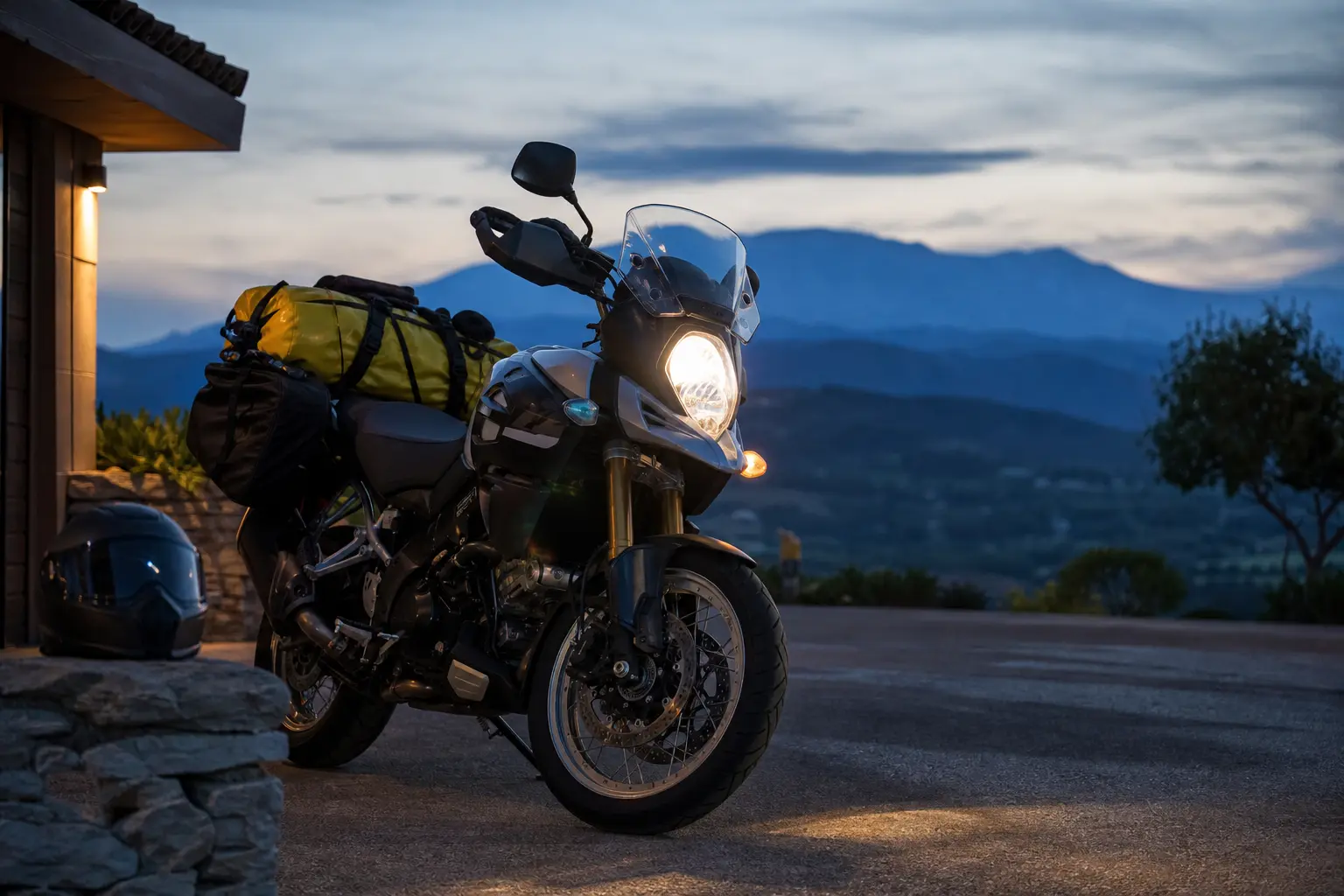 Motorcycle parked at dusk with headlight illuminating the driveway