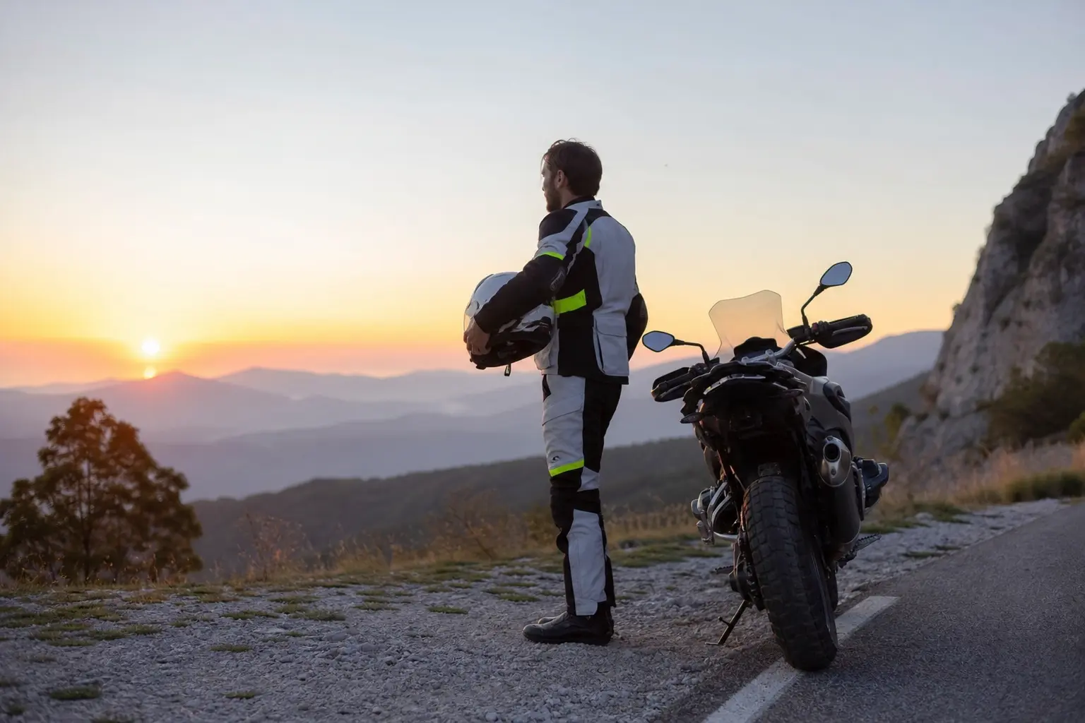 Motorcyclist in high-contrast riding gear preparing beside a motorcycle at dawn